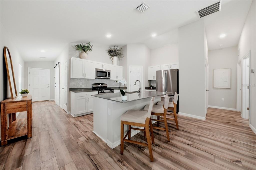 A modern kitchen features white cabinetry, a gray island with bar stools, and wood flooring — 5560 SUMMER SUNSET DRIVE, APOLLO BEACH, FL