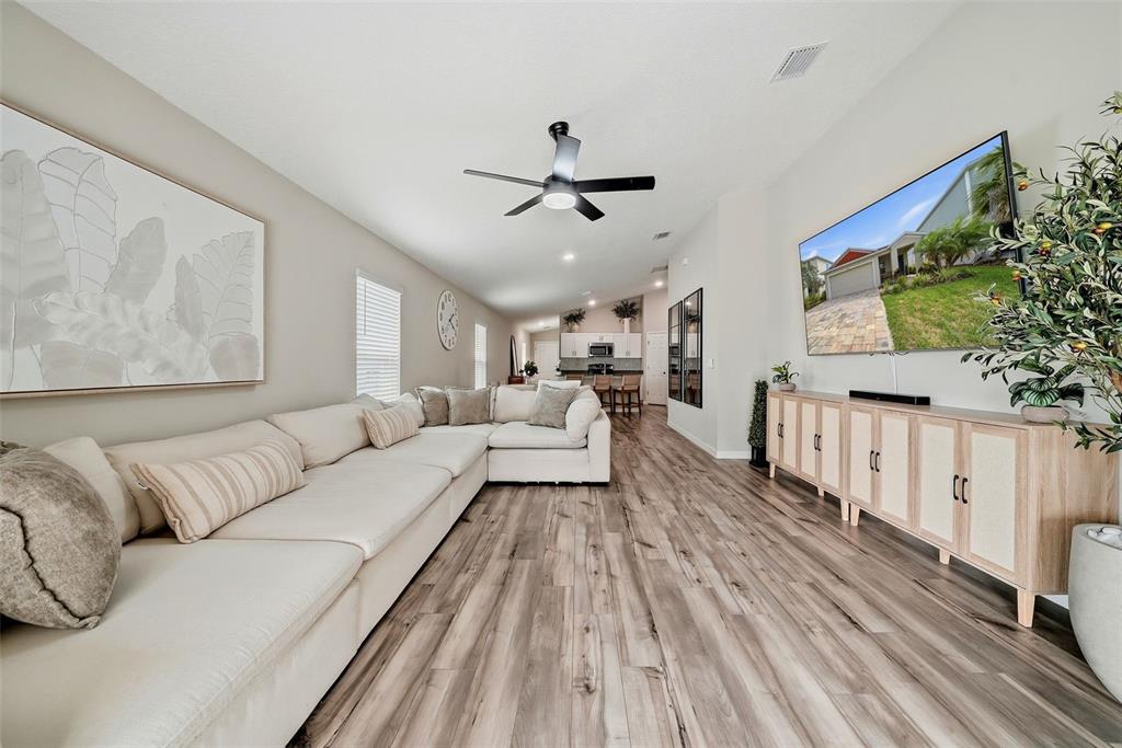 A living room features a large sectional sofa, a television, and wood-look flooring — 5560 SUMMER SUNSET DRIVE, APOLLO BEACH, FL