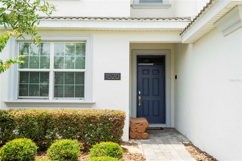 A white house exterior features a blue front door, a house number, and a hedge — 1520 FLANGE DRIVE, DAVENPORT, FL