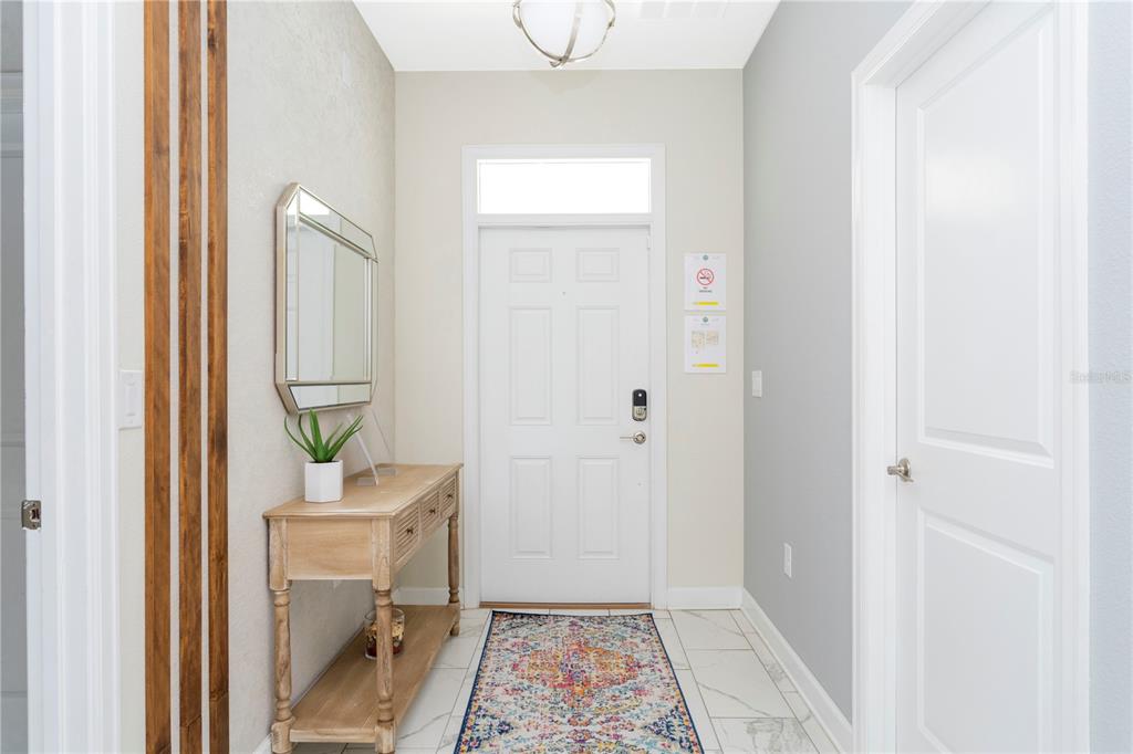 A bright entryway features a white door, a wooden console table, and a patterned runner rug — 1520 FLANGE DRIVE, DAVENPORT, FL