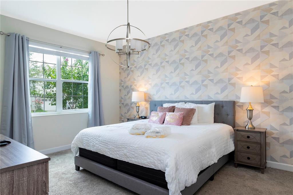 A bedroom features a bed with a patterned accent wall, gray curtains, and a chandelier — 1520 FLANGE DRIVE, DAVENPORT, FL
