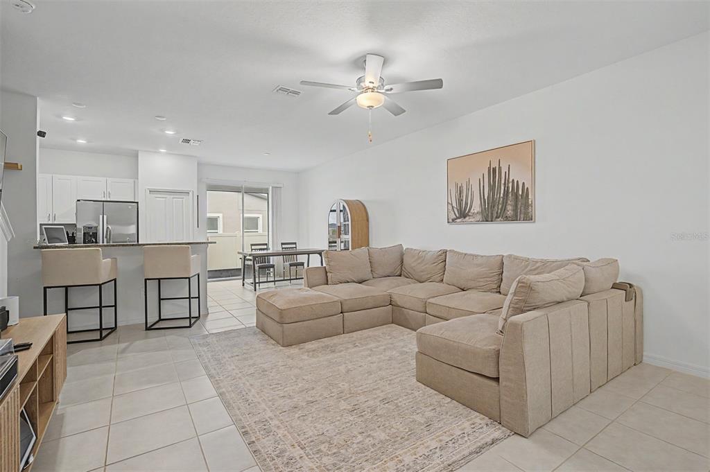 An open-concept living room features a large beige sectional sofa, tile flooring, and kitchen bar — 10261 HONEY HAMMOCK WAY, SAN ANTONIO, FL