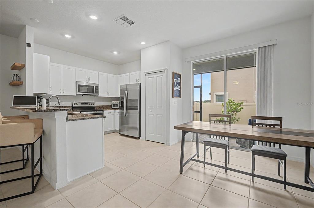 A kitchen with white cabinets and stainless steel appliances opens to a dining area — 10261 HONEY HAMMOCK WAY, SAN ANTONIO, FL
