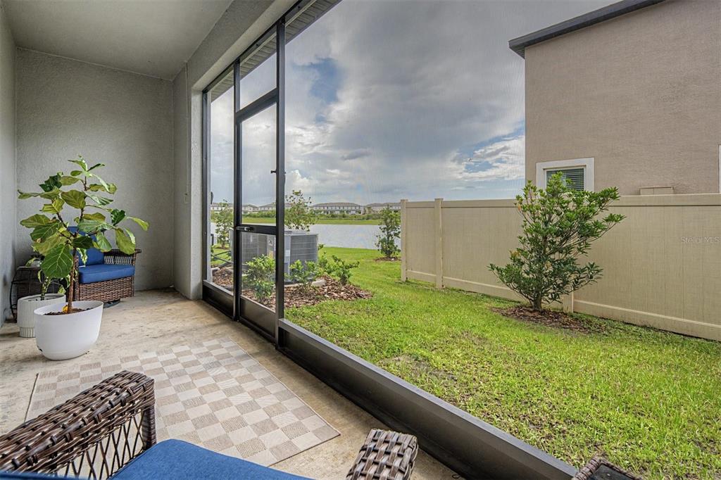 A screened-in patio overlooks a grassy yard, a fence, and a lake — 10261 HONEY HAMMOCK WAY, SAN ANTONIO, FL