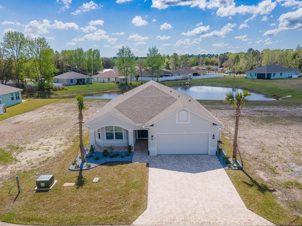 An aerial view shows a single-story house with a paved driveway and a backyard pond — 8 LAKELAND WAY, PALM COAST, FL