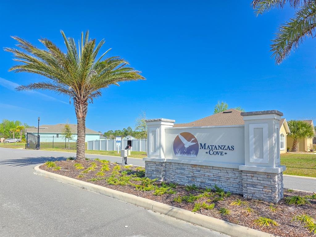 A stone and stucco entrance sign for Matanzas Cove stands beside a palm tree — 8 LAKELAND WAY, PALM COAST, FL