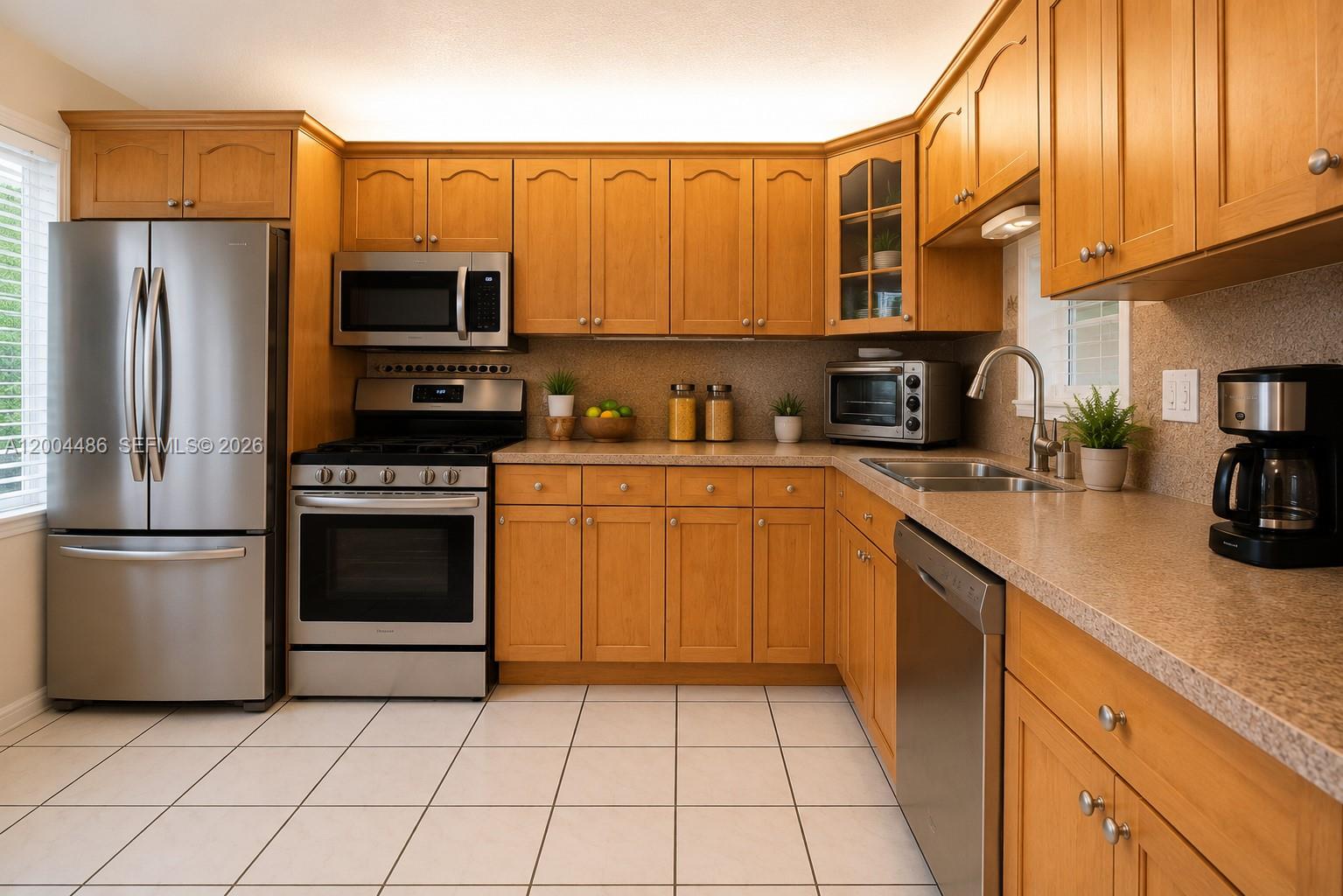 A kitchen features light wood cabinets, stainless steel appliances, and beige countertops over tiled floors — 15071 SW 127th Ct, Miami FL 33186, MIAMI, FL