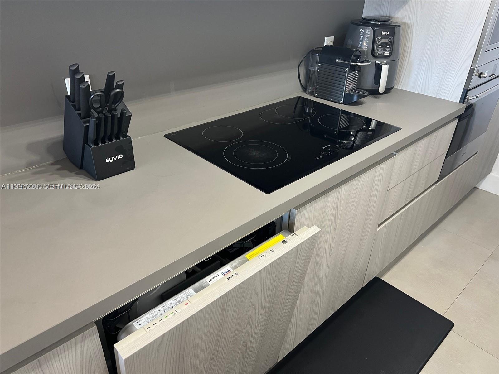 A modern kitchen features a black induction cooktop, a knife block, and an open dishwasher — 100 Lincoln Rd # 620, Miami Beach FL 33139, MIAMI BEACH, FL