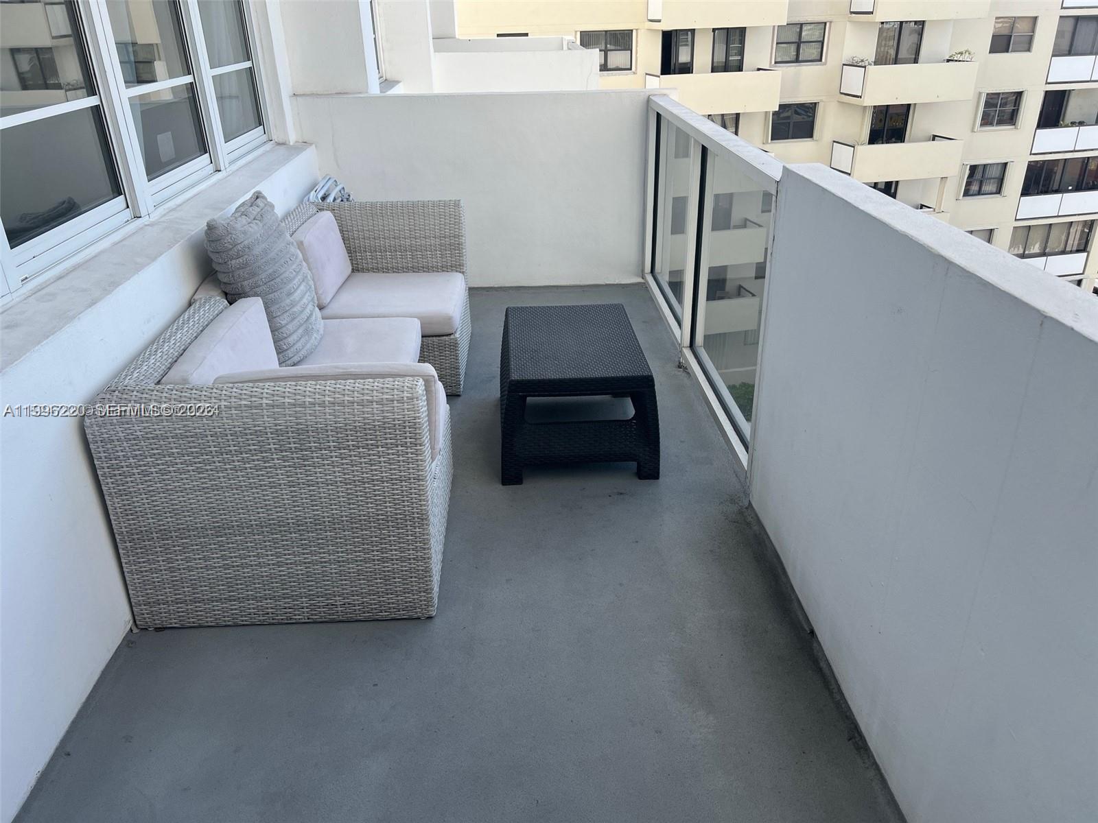 A balcony features a light-colored wicker sectional sofa and a small black coffee table — 100 Lincoln Rd # 620, Miami Beach FL 33139, MIAMI BEACH, FL