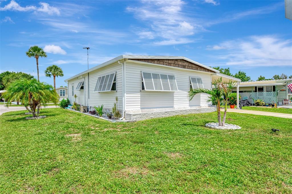 A white mobile home with shuttered windows sits on a grassy lot with palm trees — 6639 VISTA LANE, NORTH PORT, FL