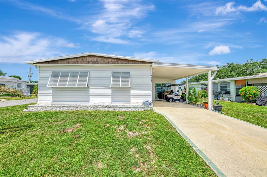 A white mobile home with a carport and a golf cart parked in the driveway — 6639 VISTA LANE, NORTH PORT, FL