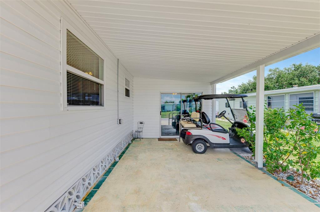 A white-sided carport features a concrete floor, a golf cart, and a sliding glass door — 6639 VISTA LANE, NORTH PORT, FL