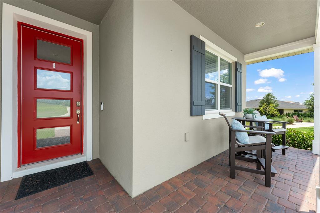 A red front door opens onto a brick-paved porch with a small table and chairs — 2790 PARK RIDGE STREET, APOPKA, FL