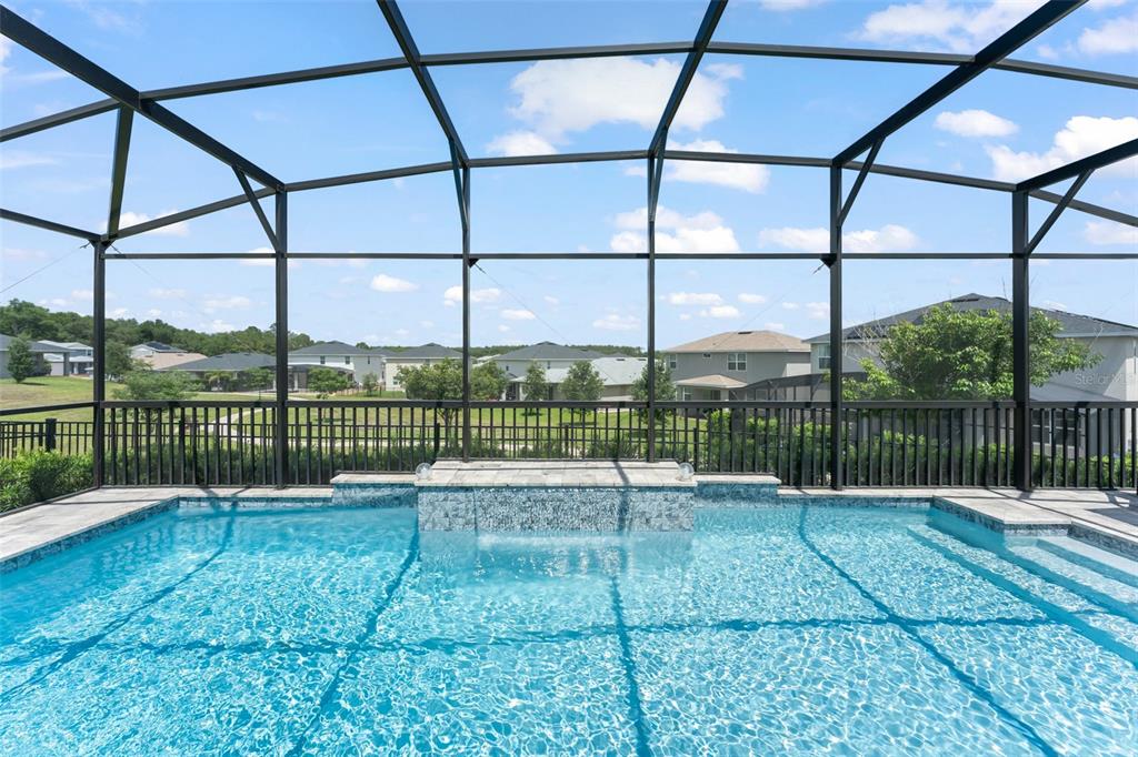 A swimming pool with a water feature sits inside a screened-in lanai overlooking a neighborhood — 2790 PARK RIDGE STREET, APOPKA, FL