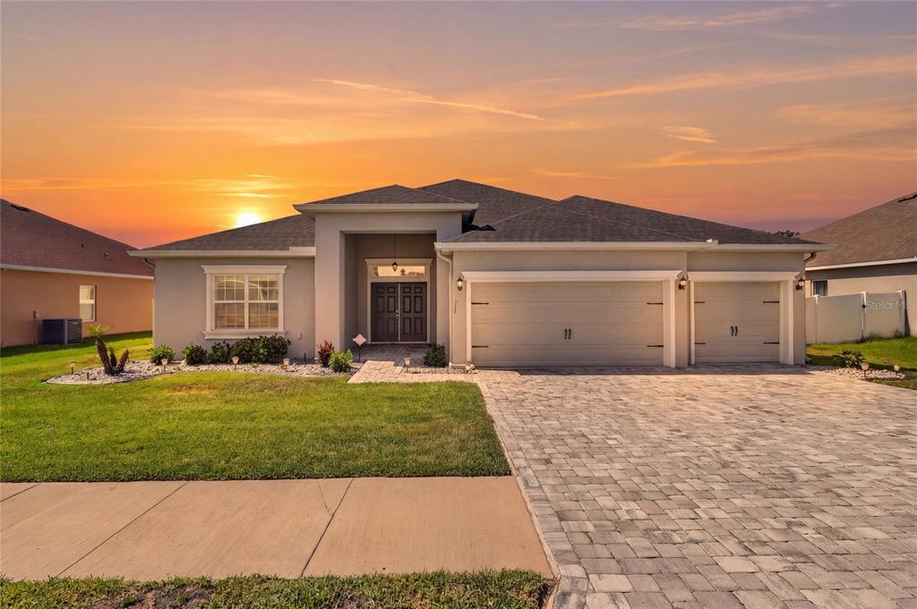 A single-story suburban house with a paved driveway and a three-car garage at sunset — 319 TRAVELERS CREEK DRIVE, AUBURNDALE, FL