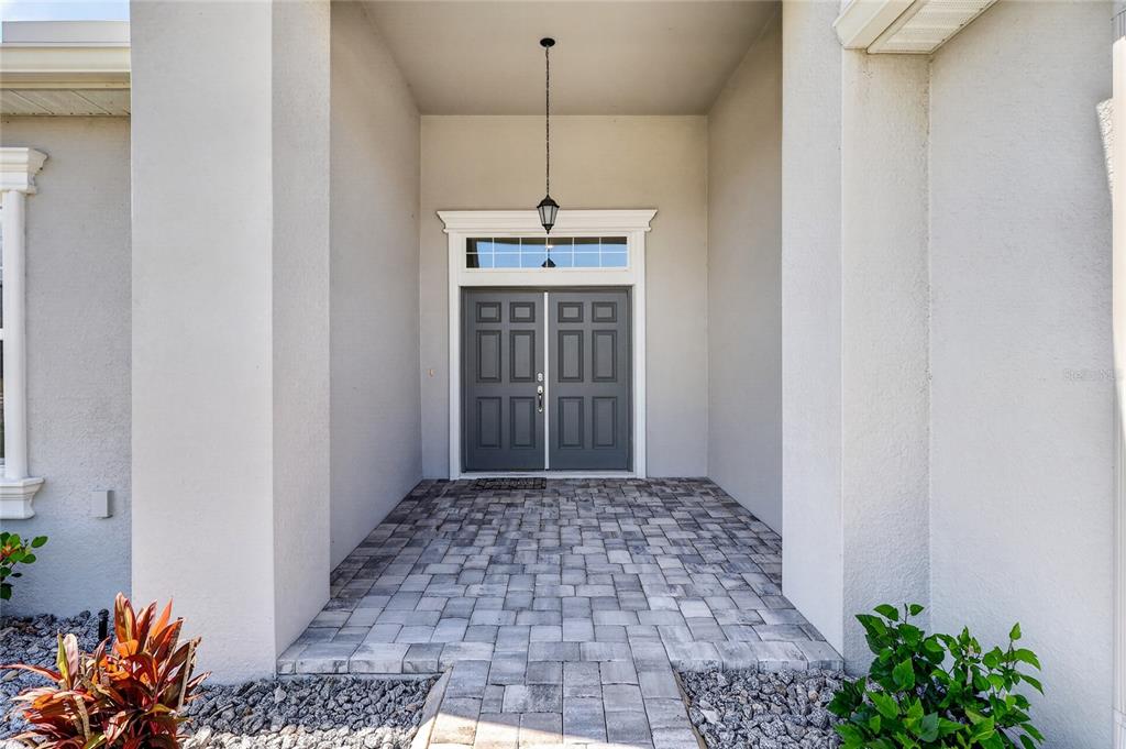 A covered entryway features a gray double door with a transom window and paver flooring — 319 TRAVELERS CREEK DRIVE, AUBURNDALE, FL