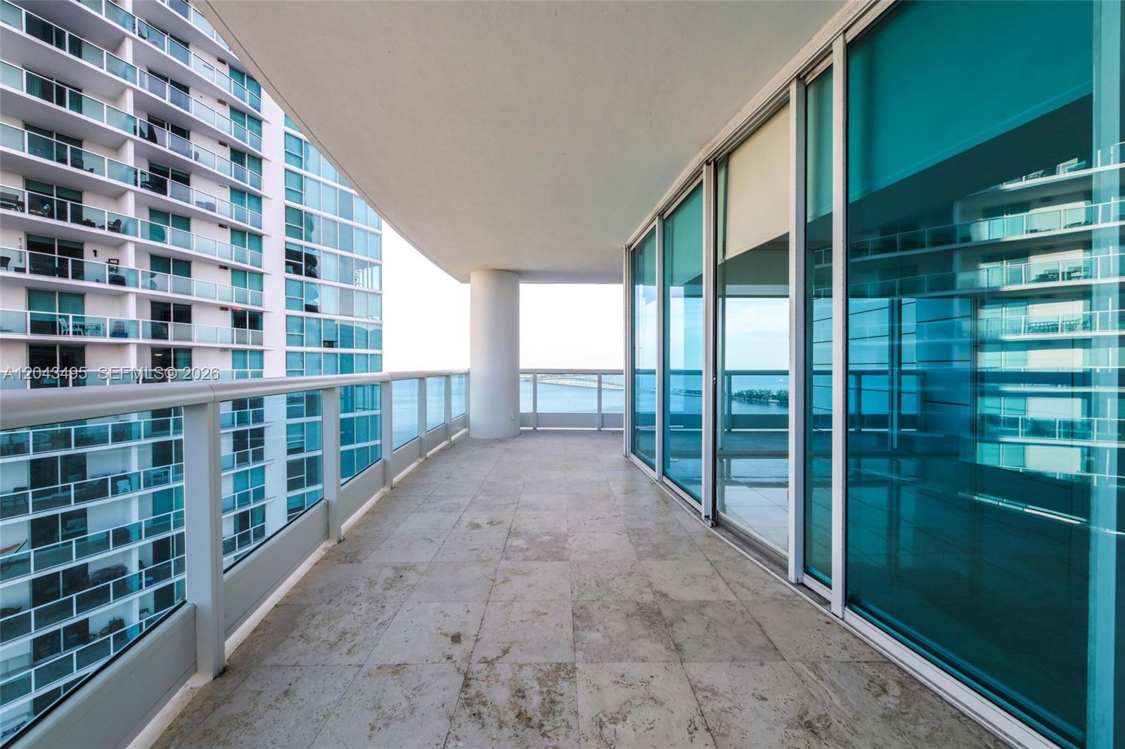 A spacious balcony with stone tile flooring overlooks the ocean and a neighboring high-rise building — 2127 Brickell Ave # 2504, Miami FL 33129, MIAMI, FL
