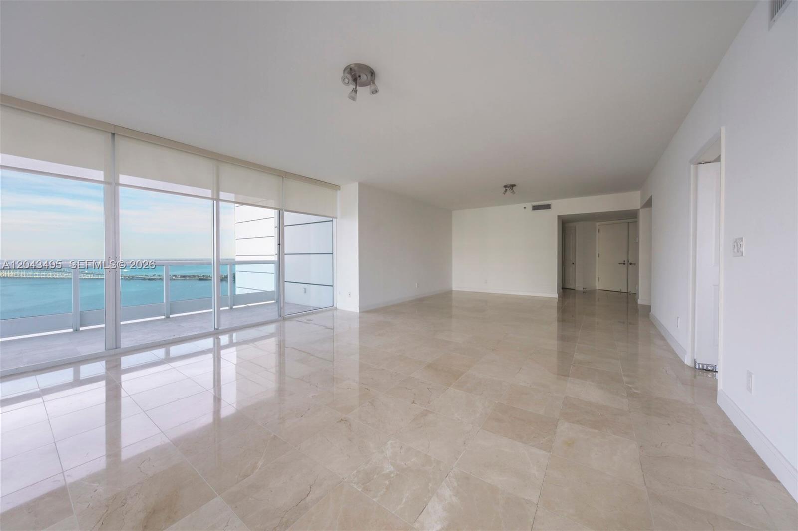 An empty living room features light-colored tile flooring, white walls, and floor-to-ceiling windows overlooking water — 2127 Brickell Ave # 2504, Miami FL 33129, MIAMI, FL