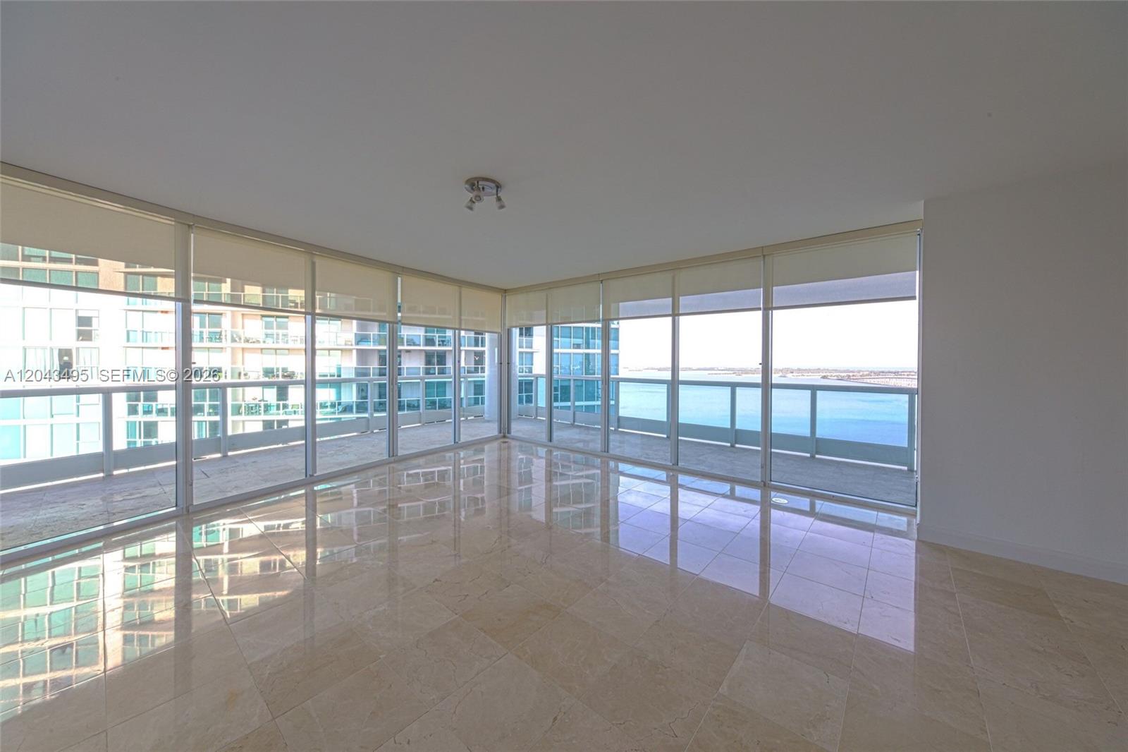 An empty room with beige tile floors, floor-to-ceiling windows, and a balcony overlooking water — 2127 Brickell Ave # 2504, Miami FL 33129, MIAMI, FL
