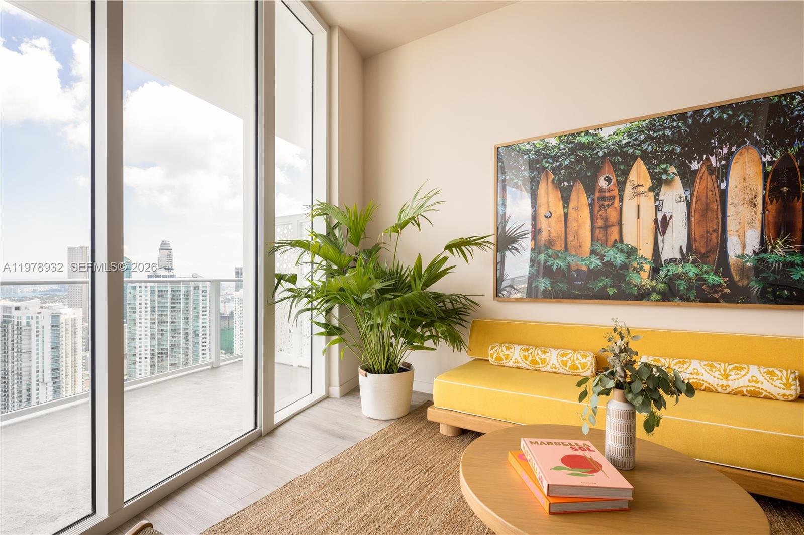 A bright living area features a yellow sofa, a large surfboard print, and balcony views — 275 SW 6th St # 2006, Miami FL 33130, MIAMI, FL