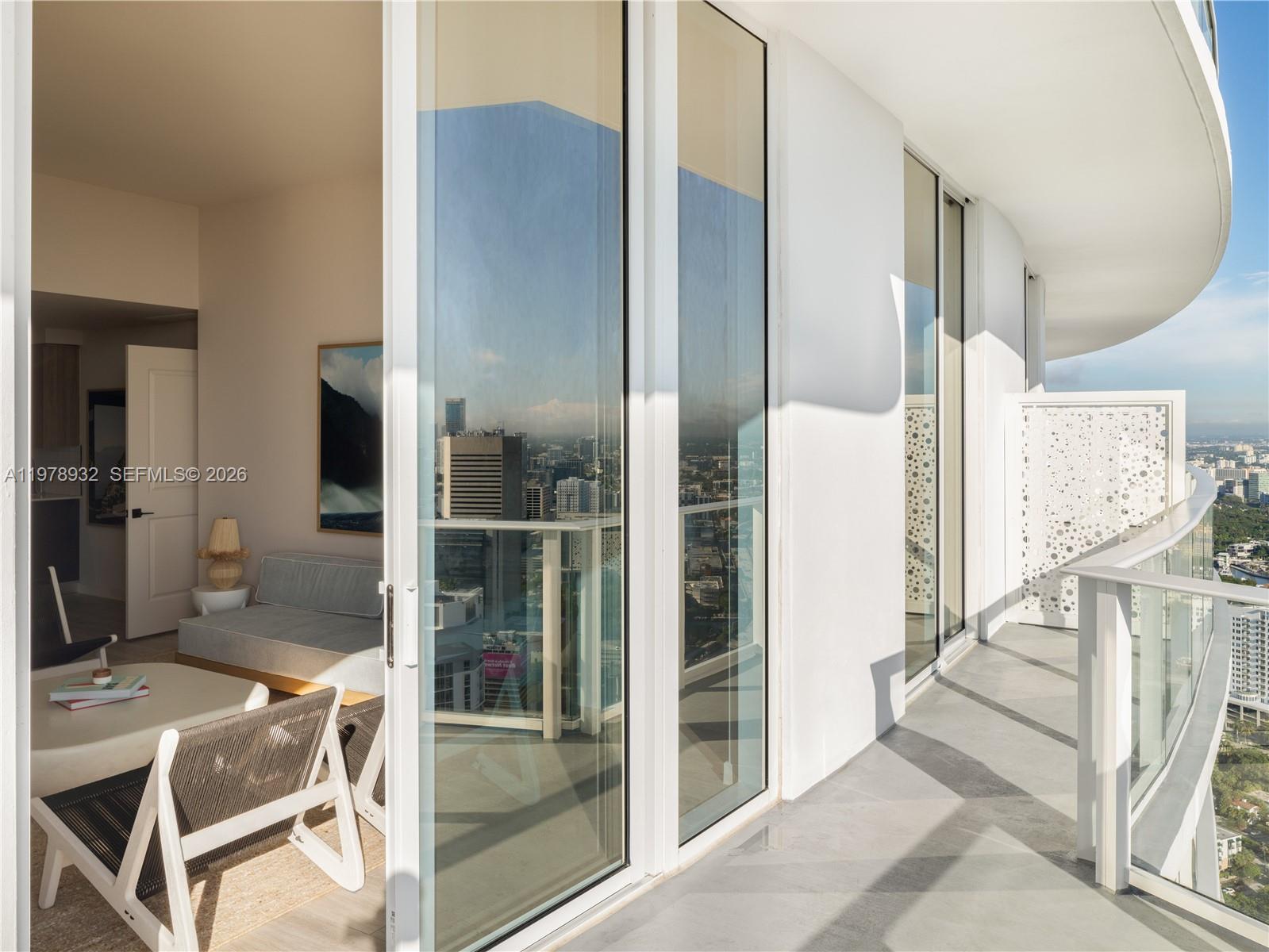 A modern balcony with glass railings overlooks a city skyline next to an interior room — 275 SW 6th St # 2006, Miami FL 33130, MIAMI, FL