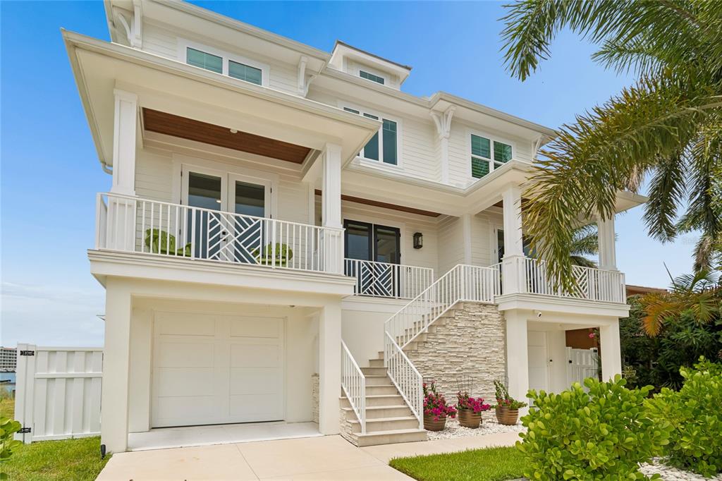 A white, elevated coastal-style house features a front staircase, a garage, and a balcony — 17715 WALL CIRCLE, REDINGTON SHORES, FL