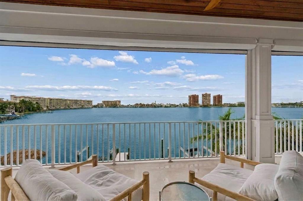 A covered balcony with lounge chairs overlooks a large body of water and distant buildings — 17715 WALL CIRCLE, REDINGTON SHORES, FL