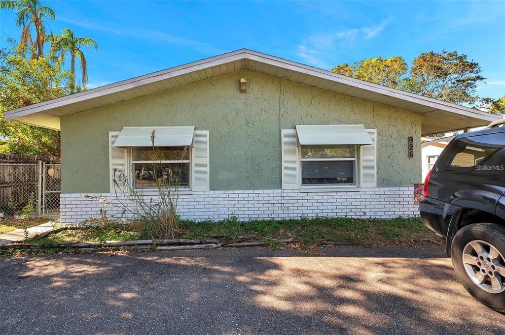A single-story house with green stucco walls, white brick trim, and two windows with awnings — 926 LAKE PALMS DRIVE, LARGO, FL