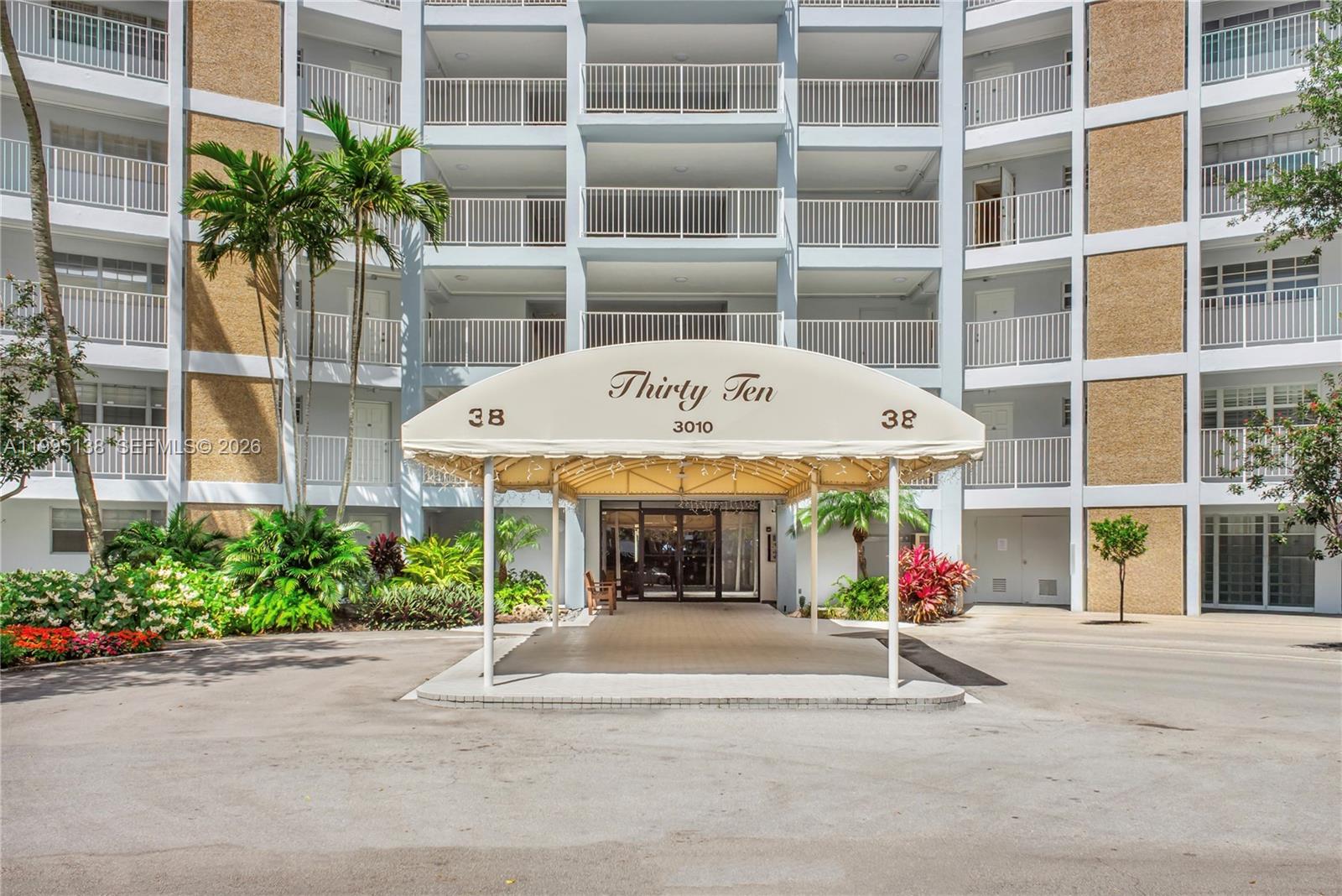 The exterior of a multi-story apartment building features a covered entrance with a beige awning — 3010 N Course Dr # 104, Pompano Beach FL 33069, POMPANO BEACH, FL