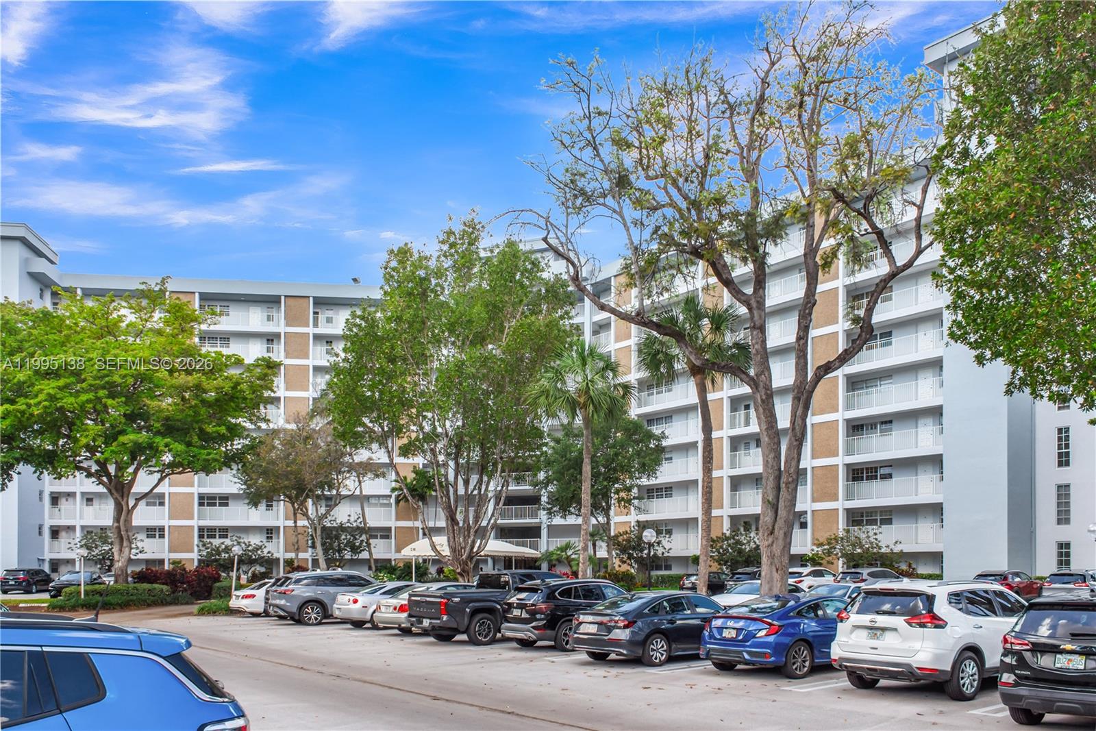 A multi-story residential apartment building stands behind a parking lot filled with various vehicles — 3010 N Course Dr # 104, Pompano Beach FL 33069, POMPANO BEACH, FL