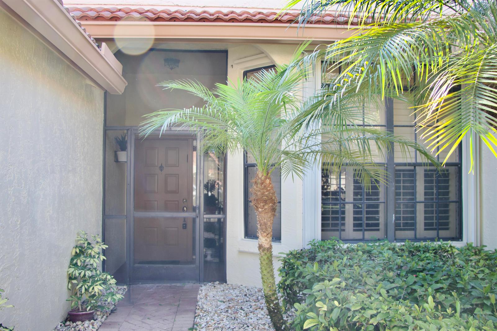 The front entrance features a brown door with a screen, a palm tree, and landscaping — 8304 Waterline Drive # 103, Boynton Beach FL 33472, BOYNTON BEACH, FL