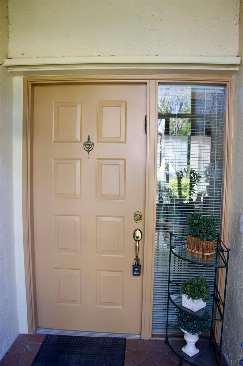 A tan front door with a side window and a small metal shelf with plants — 8304 Waterline Drive # 103, Boynton Beach FL 33472, BOYNTON BEACH, FL