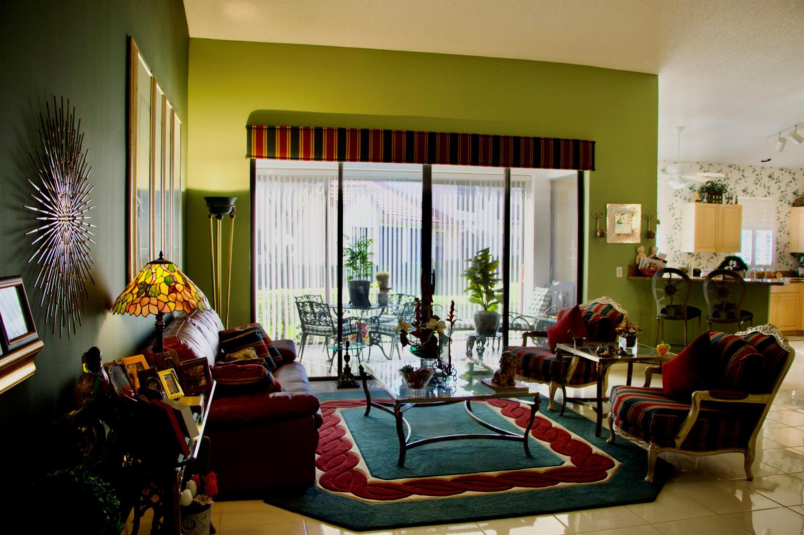 A living room with green walls, a red sofa, patterned armchairs, and sliding glass patio doors — 8304 Waterline Drive # 103, Boynton Beach FL 33472, BOYNTON BEACH, FL