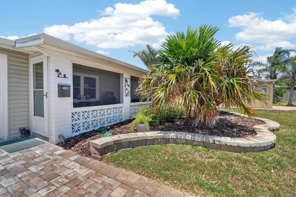 A white mobile home exterior features a screened porch, a palm tree, and a stone planter — 6 TROPICAL DRIVE, ORMOND BEACH, FL