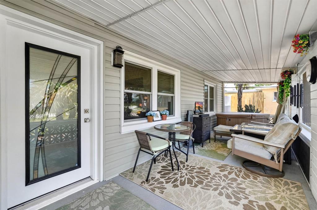 A covered porch features a glass-paneled door, a small dining set, and a hot tub — 6 TROPICAL DRIVE, ORMOND BEACH, FL
