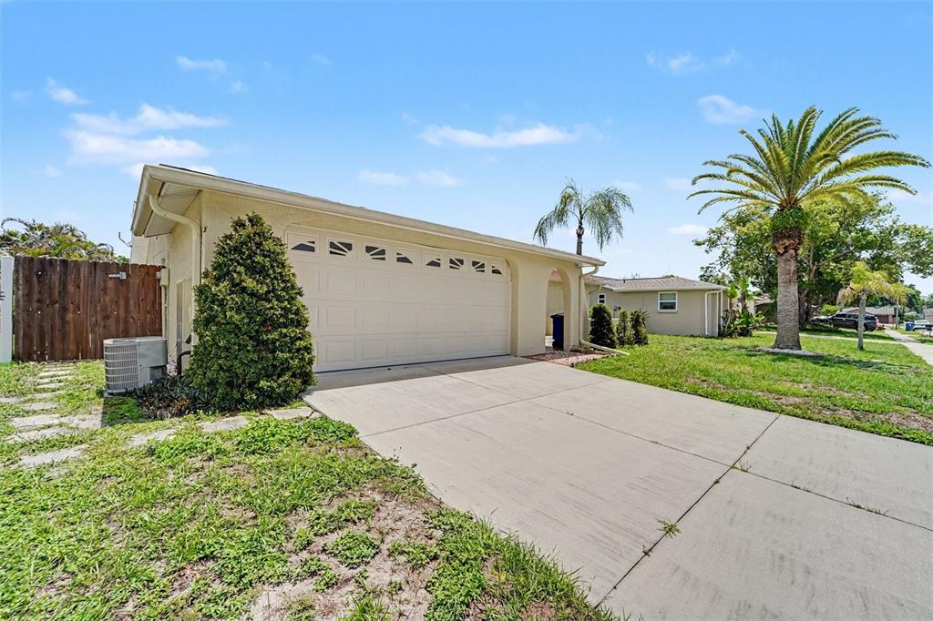 A beige house exterior with a two-car garage, concrete driveway, and a palm tree — 4316 CHIPMUNK DRIVE, NEW PORT RICHEY, FL