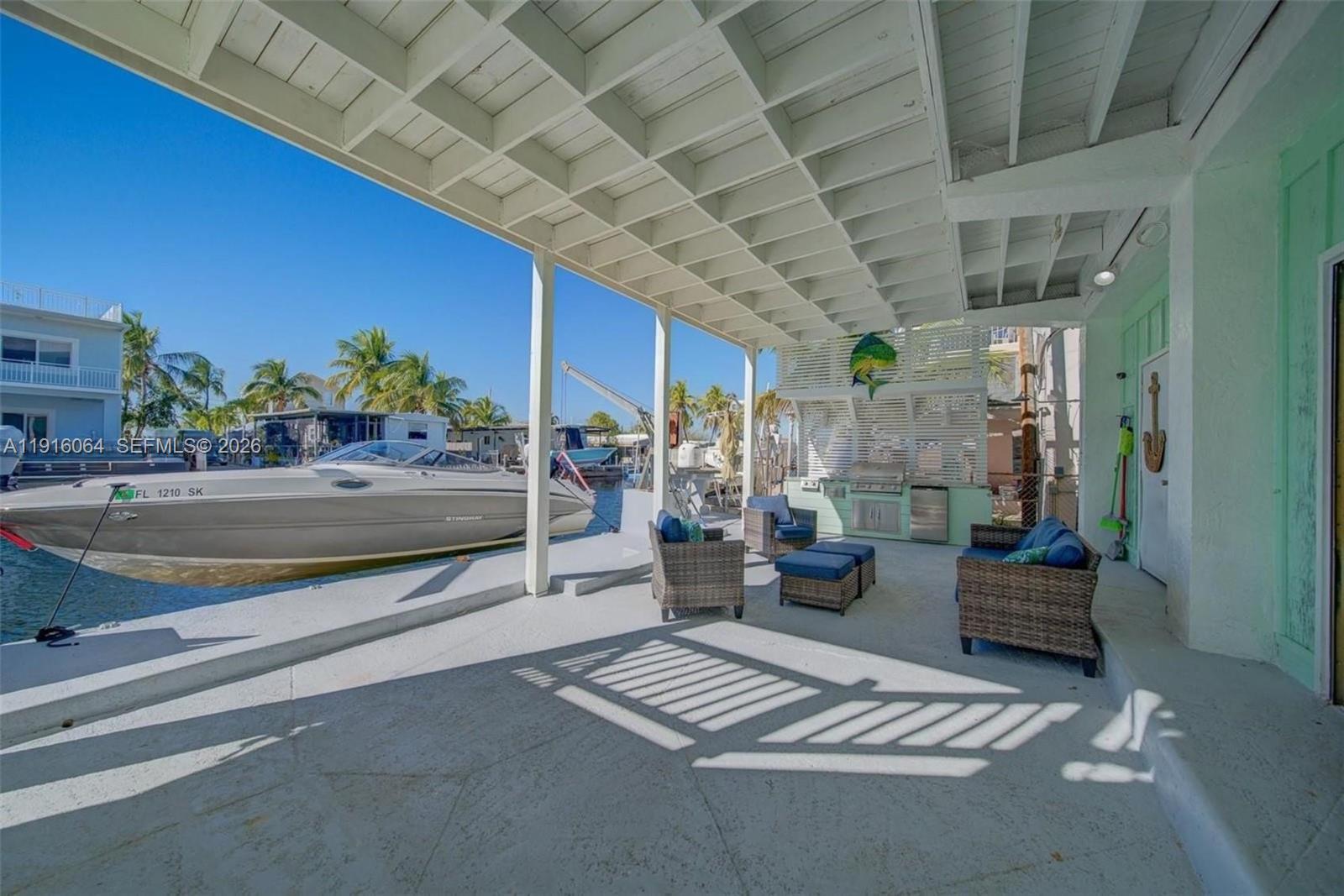 A covered patio features outdoor seating, a built-in grill, and a boat docked alongside — 2 Snipe Rd, Key Largo FL 33037, KEY LARGO, FL