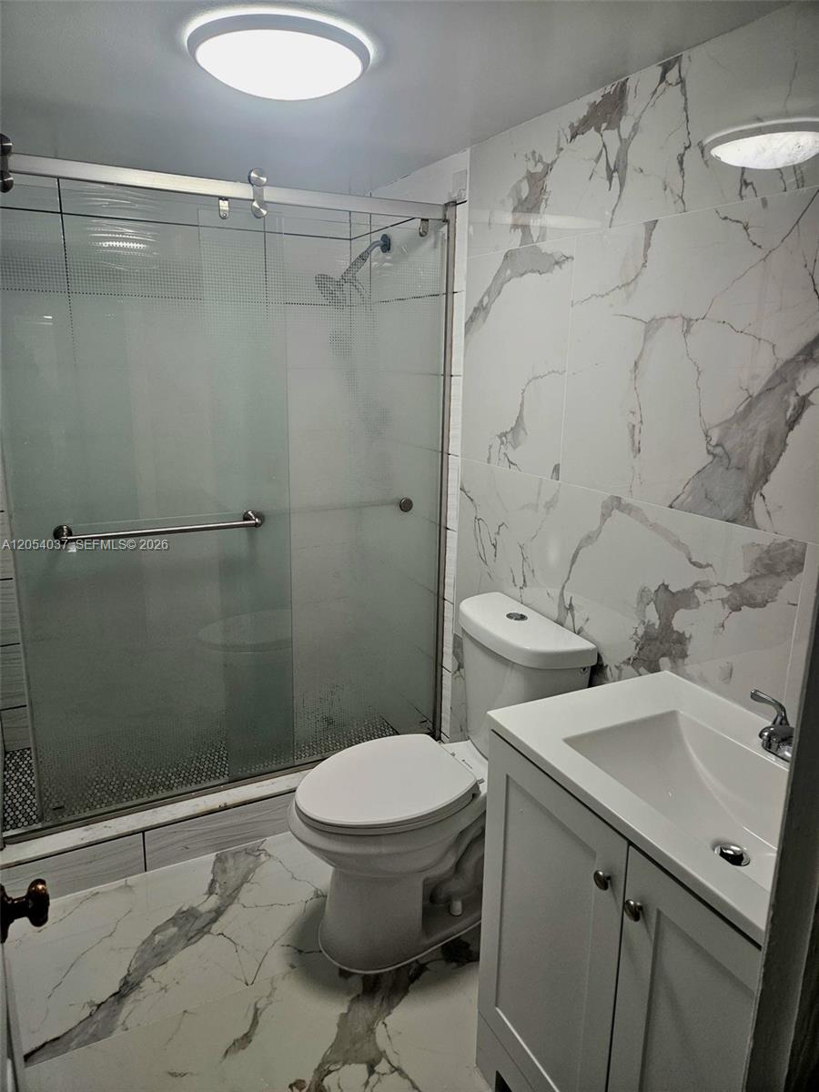 A bathroom features a glass-enclosed shower, white toilet, and vanity with marble-patterned tile flooring — 2950 Kirk Rd # 2950, Lake Worth FL 33461, LAKE WORTH, FL