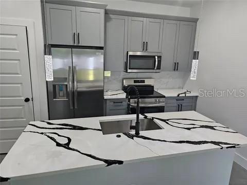 A modern kitchen features gray cabinets, stainless steel appliances, and a white marble-patterned island countertop — 0 ROBINSON DRIVE, HAINES CITY, FL
