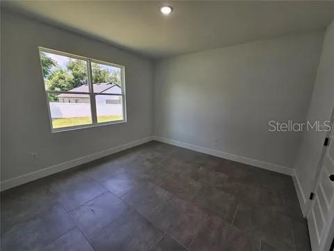 An empty bedroom features light gray walls, large tile flooring, and a window overlooking a yard — 0 ROBINSON DRIVE, HAINES CITY, FL