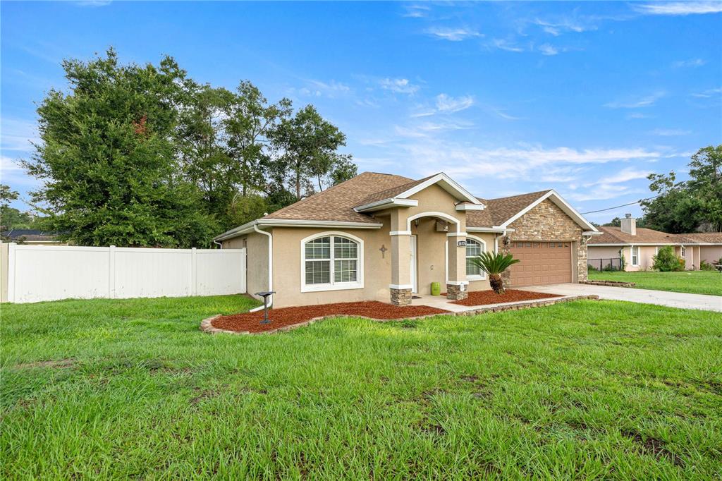 A single-story house with a tan stucco exterior, stone accents, and a two-car garage — 16376 SE 81ST COURT, SUMMERFIELD, FL