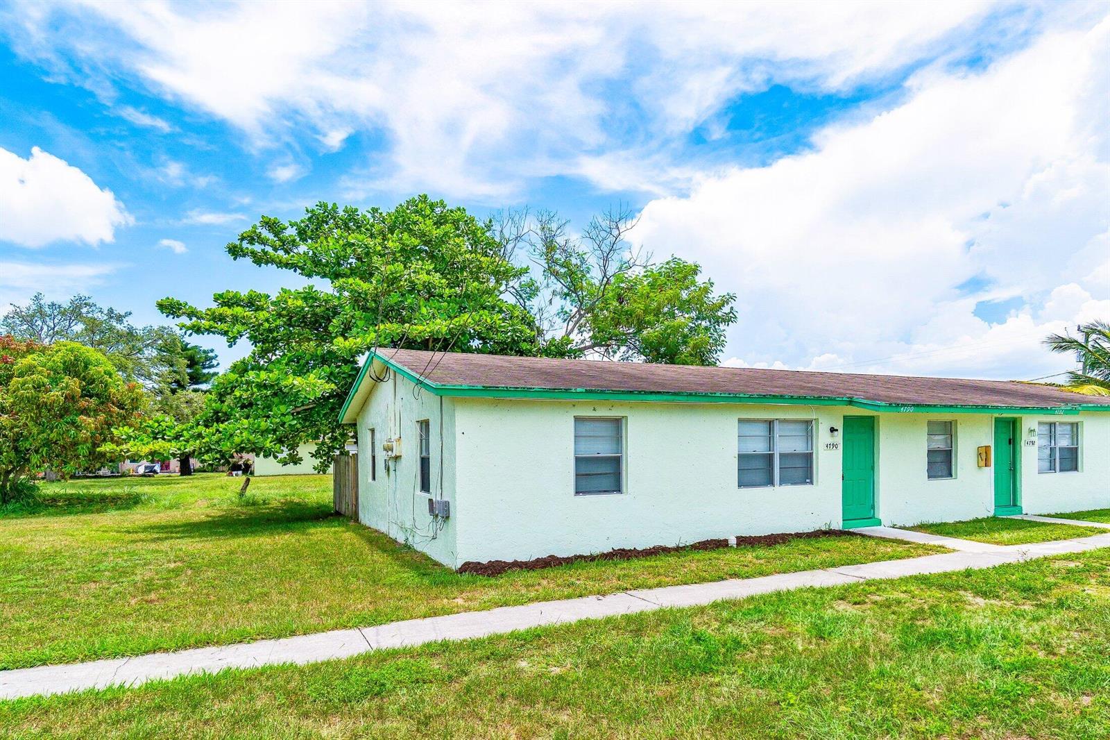 A single-story light green duplex with two front doors and a sidewalk under a blue sky — 4790 Gulfstream Road, FL 33461, FL