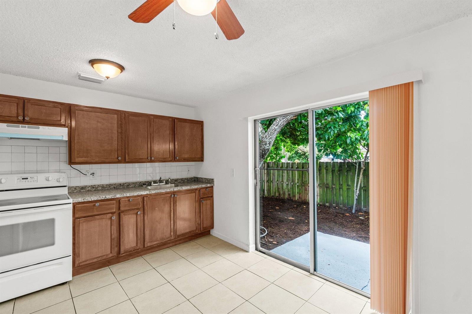 A kitchen with wood cabinets, white appliances, and tile floors opens to a small patio — 4790 Gulfstream Road, FL 33461, FL