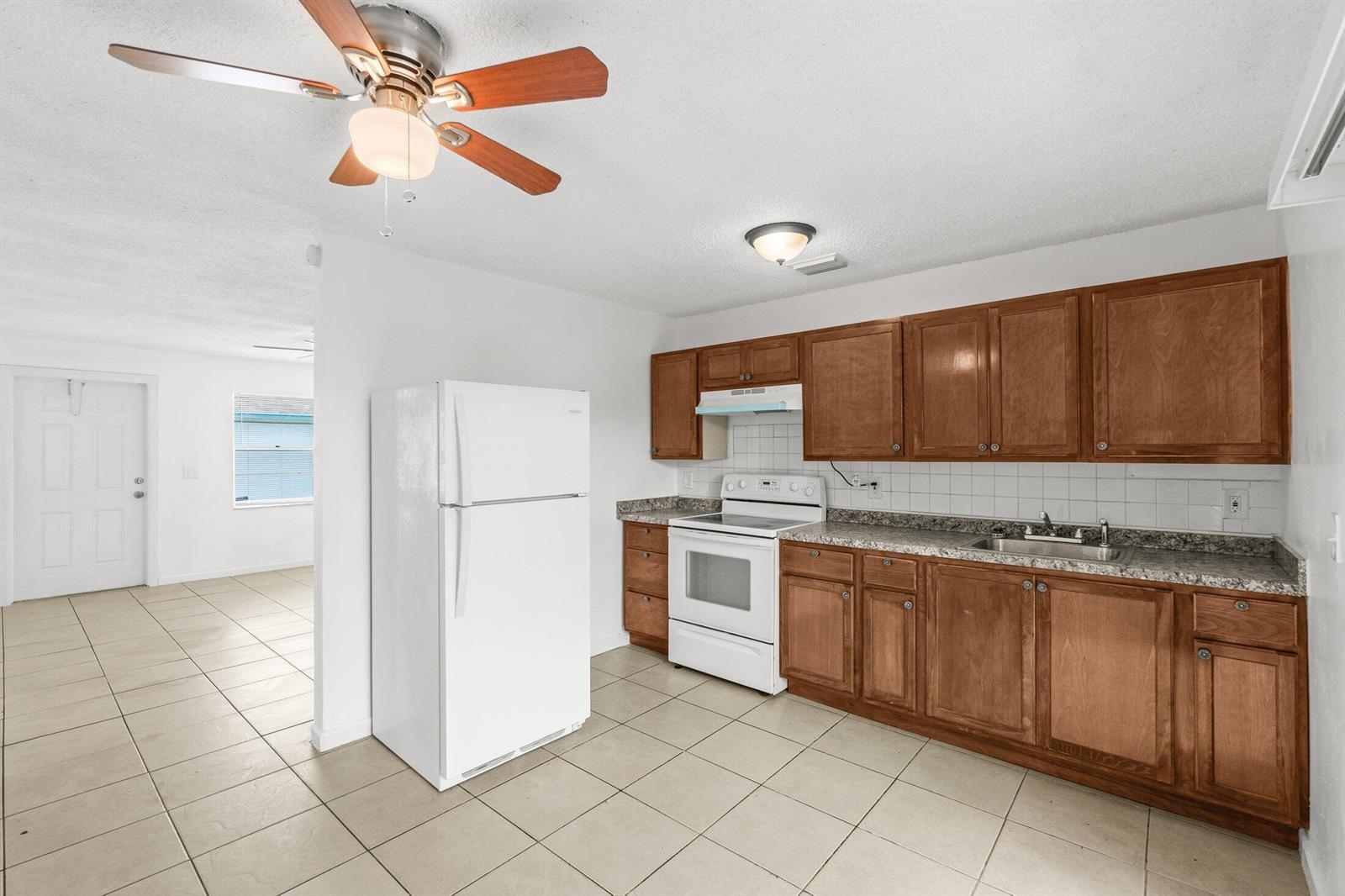 A kitchen features wooden cabinets, granite-look countertops, white appliances, and light-colored floor tiles — 4790 Gulfstream Road, FL 33461, FL