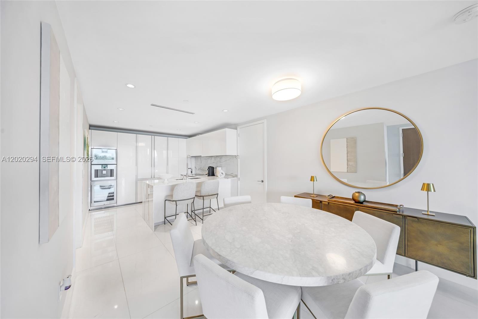 A modern dining area with a marble table and kitchen island features white glossy cabinets — 10201 Collins Ave # 305, Bal Harbour FL 33154, BAL HARBOUR, FL