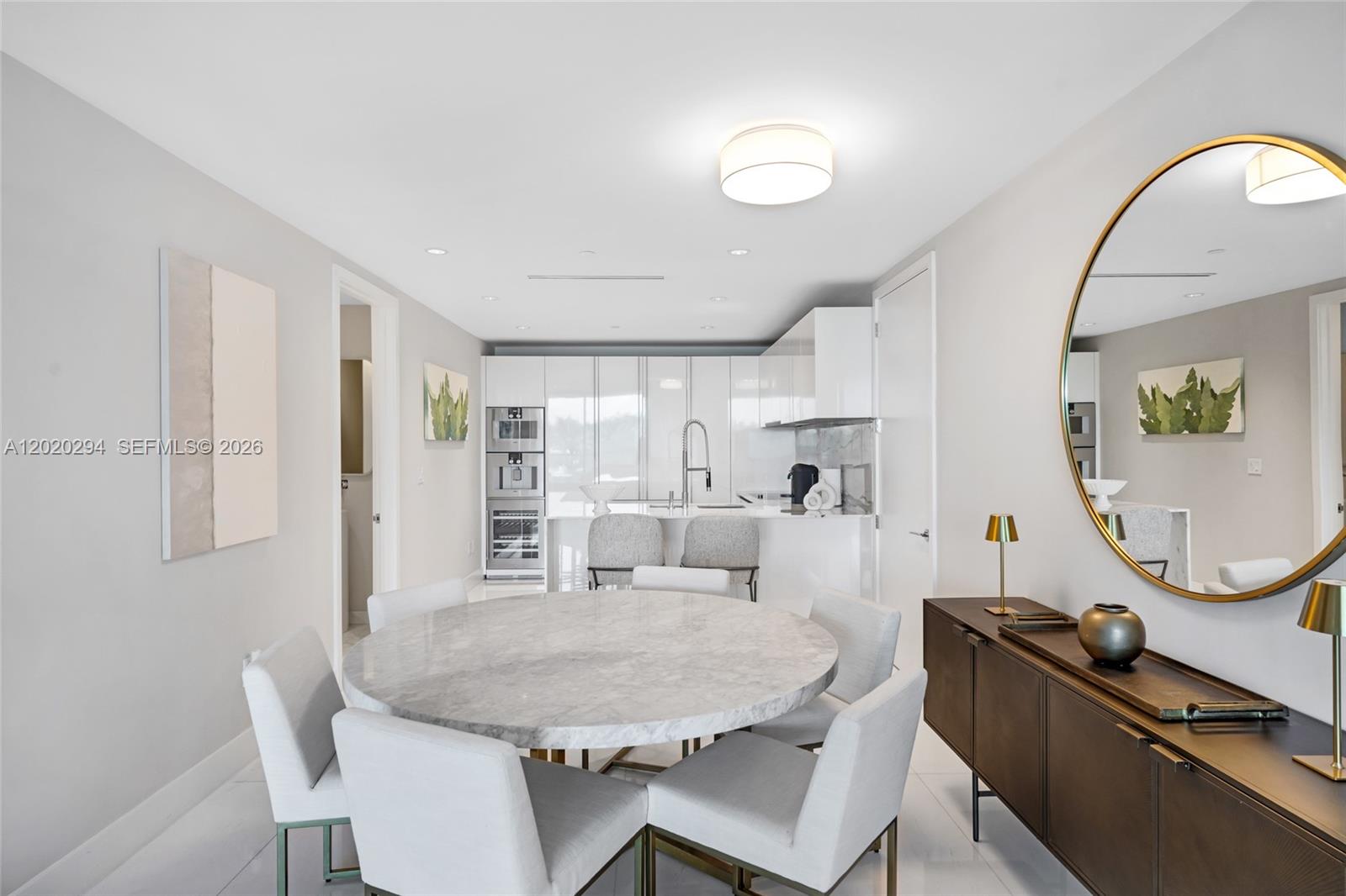 A dining area with a round marble table and chairs sits before a modern kitchen — 10201 Collins Ave # 305, Bal Harbour FL 33154, BAL HARBOUR, FL