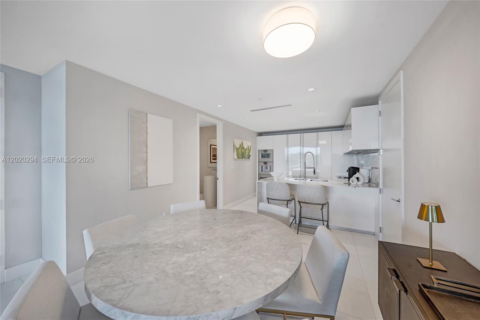 A modern kitchen and dining area feature a marble table, white cabinets, and tile flooring — 10201 Collins Ave # 305, Bal Harbour FL 33154, BAL HARBOUR, FL