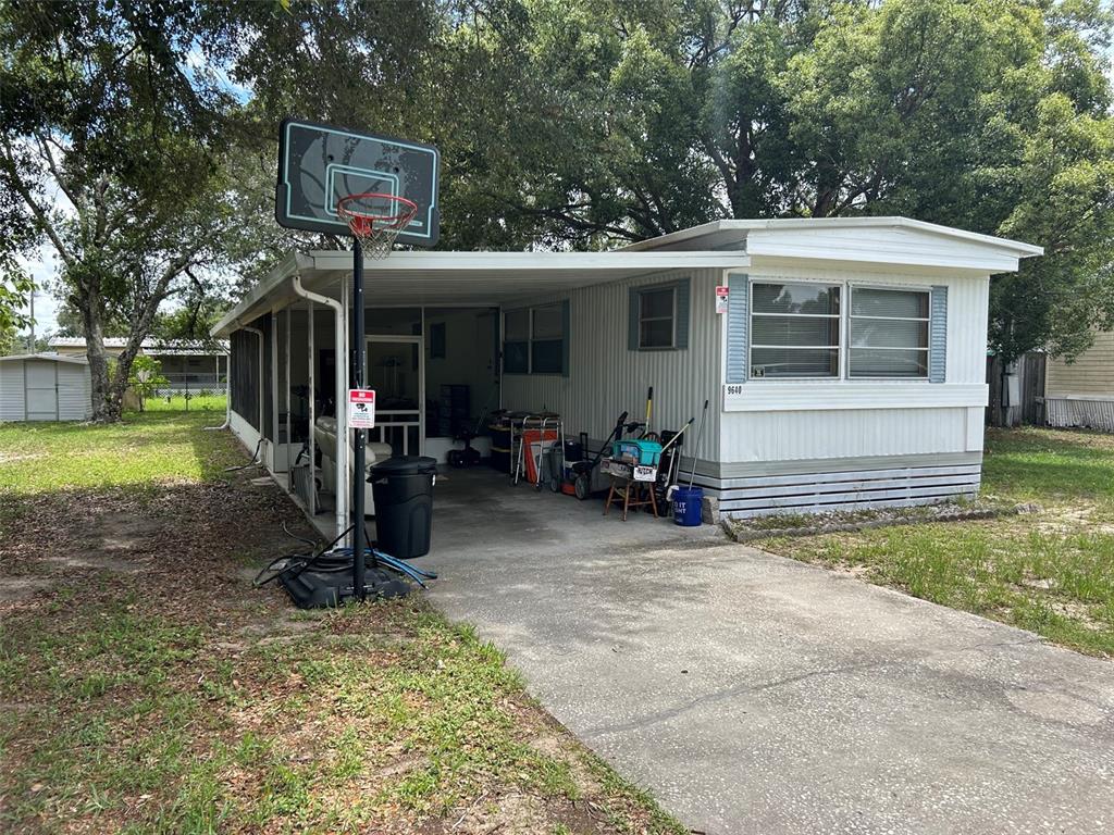 A single-story mobile home with a carport, screened porch, and a basketball hoop in front — 16716 SE 101ST COURT ROAD, SUMMERFIELD, FL