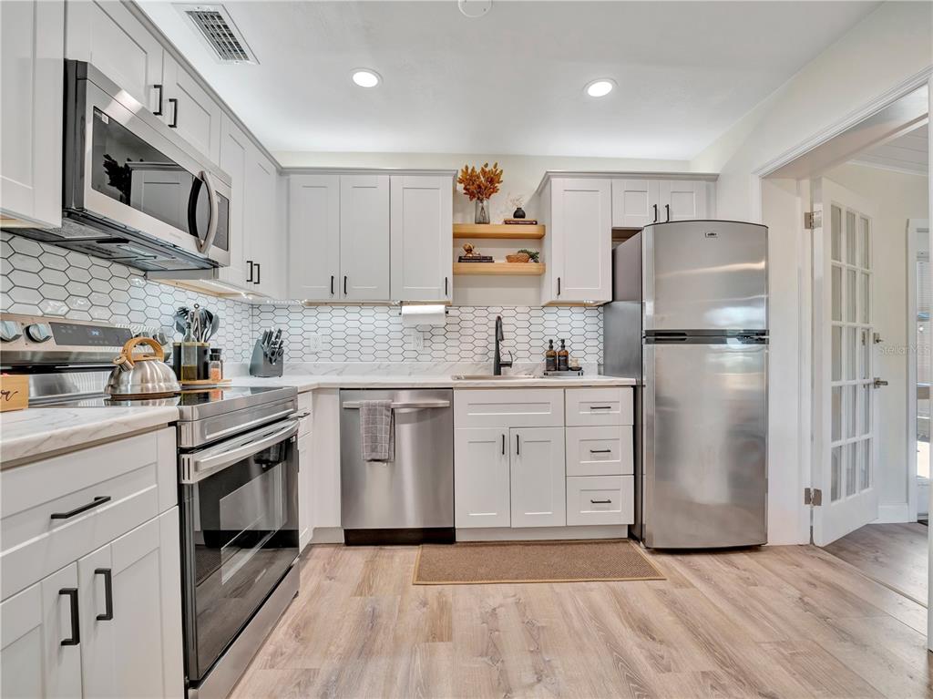 A kitchen features white cabinets, stainless steel appliances, a hexagon tile backsplash, and wood flooring — 4002 W OKLAHOMA AVENUE, TAMPA, FL