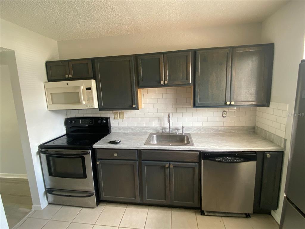 A kitchen features dark cabinets, stainless steel appliances, a light countertop, and a white backsplash — 22707 WATERSEDGE BOULEVARD UNIT 57, LAND O LAKES, FL